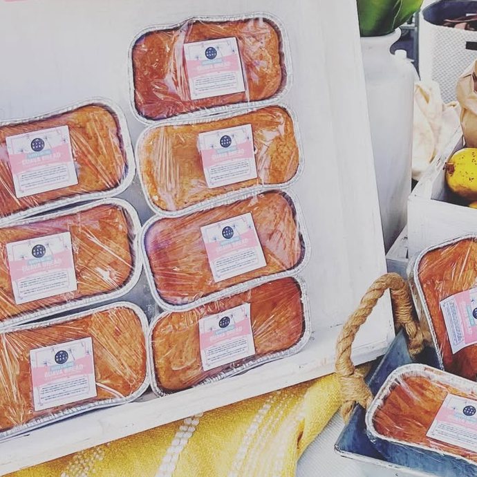 Loaves and paper bags of guava in a white crate at the market table